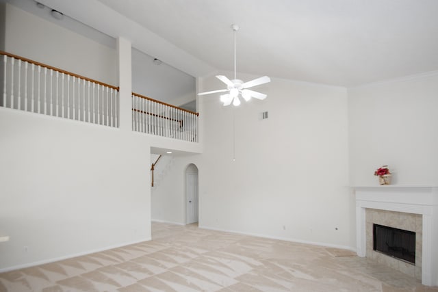 unfurnished living room with ceiling fan, ornamental molding, light carpet, a fireplace, and a towering ceiling