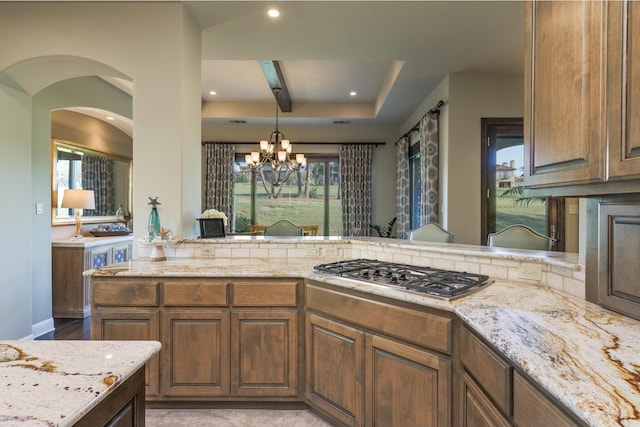 kitchen with a notable chandelier, decorative light fixtures, light stone countertops, and stainless steel gas cooktop