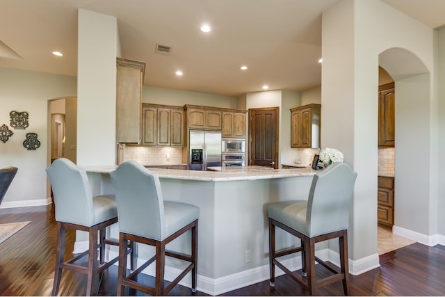 kitchen featuring built in appliances, dark hardwood / wood-style floors, a kitchen breakfast bar, and kitchen peninsula