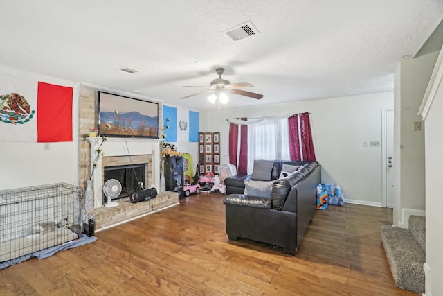 living room with a brick fireplace, ceiling fan, hardwood / wood-style flooring, and a textured ceiling