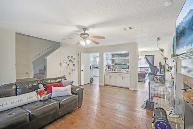 living room featuring light hardwood / wood-style flooring, ceiling fan, and a textured ceiling