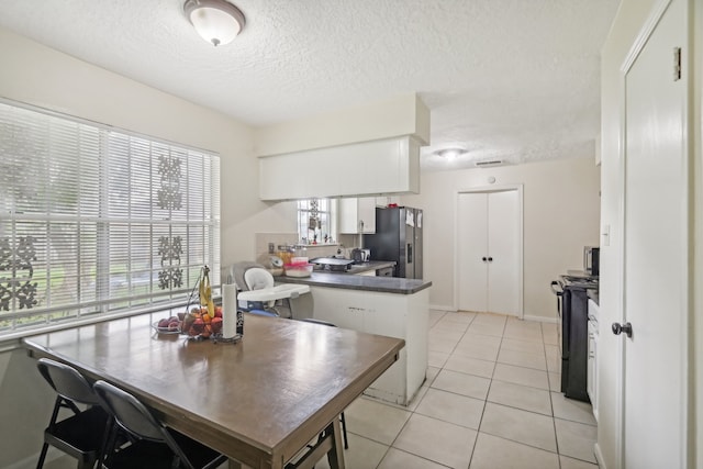 kitchen featuring a textured ceiling, white cabinets, light tile patterned floors, black electric range oven, and stainless steel fridge