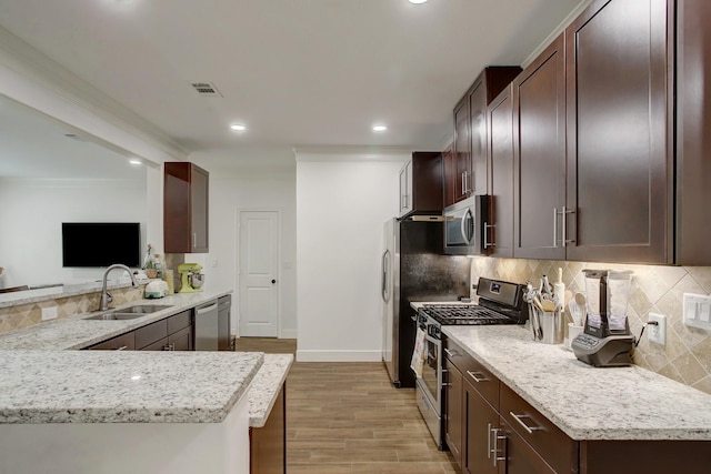 kitchen with sink, light stone counters, kitchen peninsula, light hardwood / wood-style floors, and appliances with stainless steel finishes