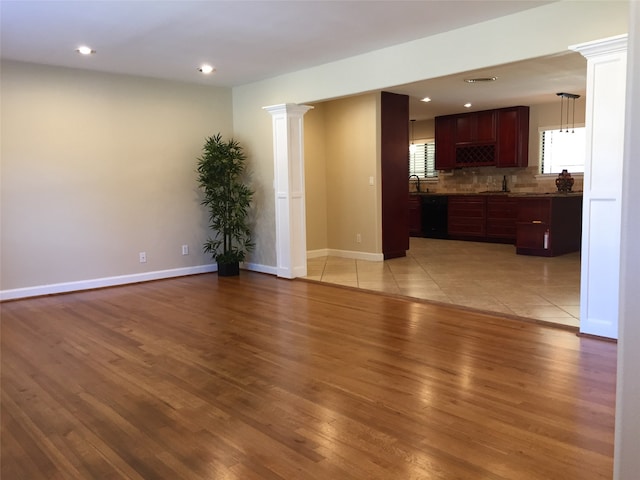 unfurnished living room with decorative columns, light hardwood / wood-style floors, and sink