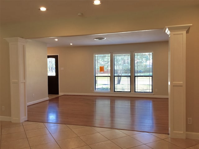 empty room with decorative columns, light hardwood / wood-style floors, and a healthy amount of sunlight