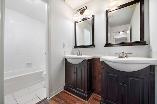 full bathroom featuring wood-type flooring, vanity, tiled shower / bath combo, and toilet