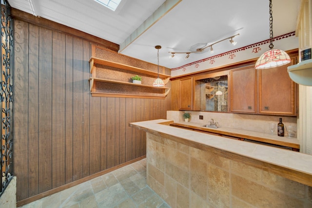 kitchen with pendant lighting, wood walls, a skylight, and sink