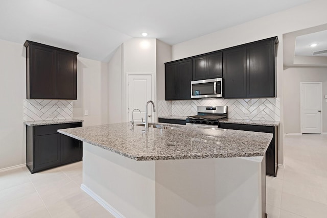 kitchen with stainless steel appliances, a kitchen island with sink, a sink, and light stone counters