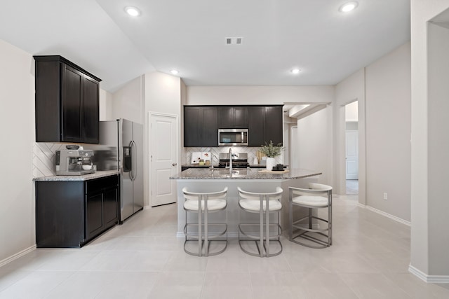 kitchen with stainless steel appliances, visible vents, a kitchen island with sink, light stone countertops, and a kitchen breakfast bar