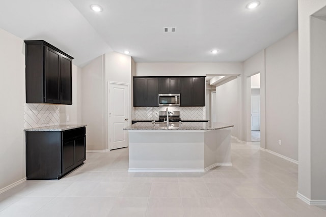 kitchen featuring a kitchen island with sink, visible vents, range, light stone countertops, and stainless steel microwave