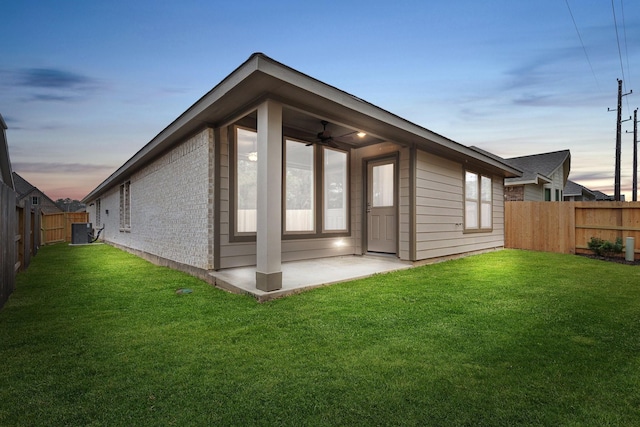 back of house at dusk with a patio area, a fenced backyard, brick siding, and a yard