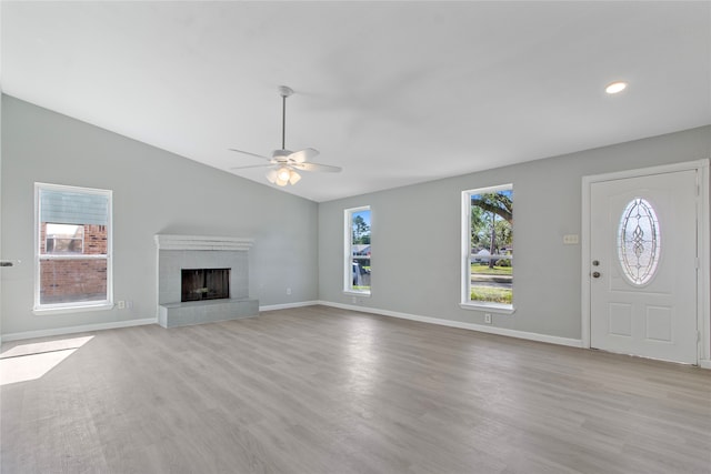 unfurnished living room featuring light hardwood / wood-style flooring, a tiled fireplace, lofted ceiling, and a wealth of natural light