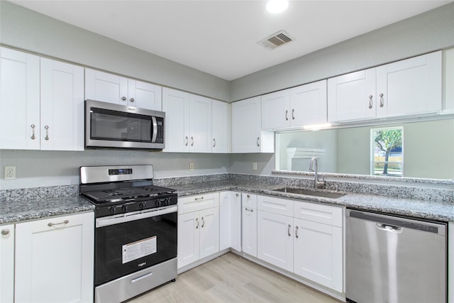 kitchen featuring sink, light hardwood / wood-style flooring, stone counters, white cabinetry, and stainless steel appliances