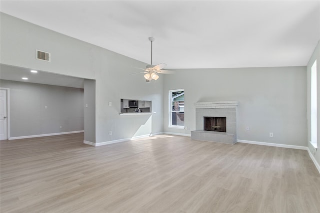 unfurnished living room with ceiling fan, light wood-type flooring, a tiled fireplace, and high vaulted ceiling