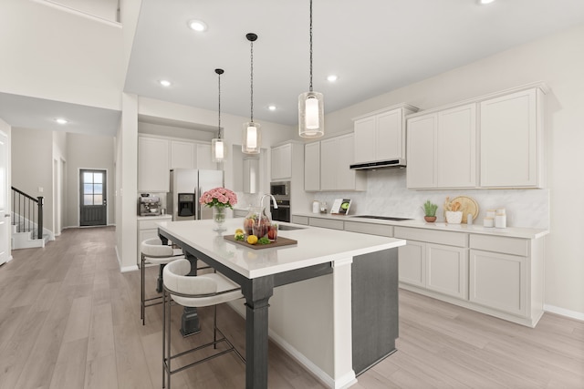 kitchen featuring hanging light fixtures, an island with sink, light hardwood / wood-style floors, white cabinets, and appliances with stainless steel finishes