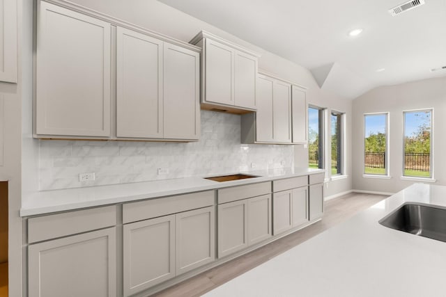 kitchen with decorative backsplash, black electric stovetop, light wood-type flooring, and vaulted ceiling