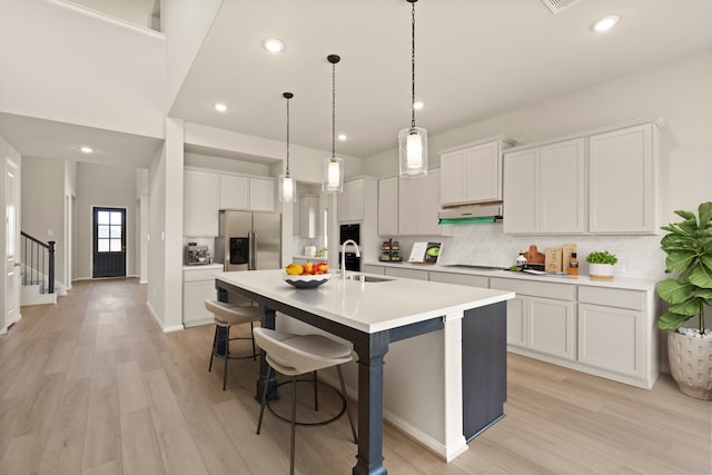 kitchen with stainless steel refrigerator with ice dispenser, white cabinetry, sink, and a center island with sink