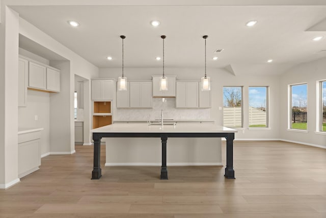 kitchen with white cabinetry, sink, tasteful backsplash, and an island with sink