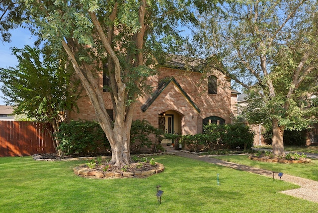 english style home with a front yard, fence, and brick siding