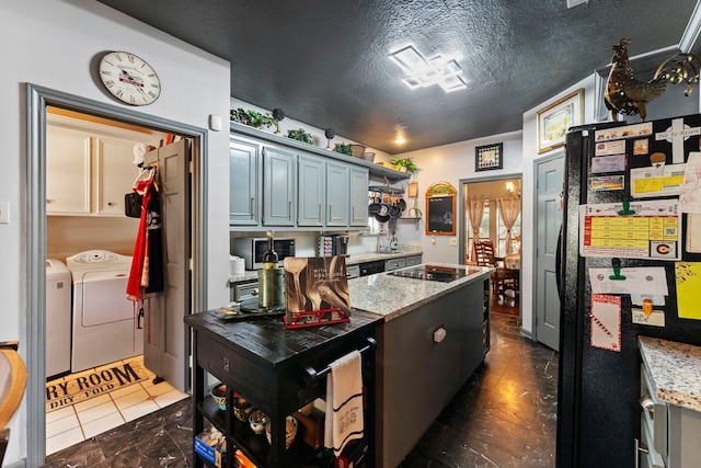 kitchen with a textured ceiling, light stone counters, dark tile patterned floors, washer and dryer, and black appliances