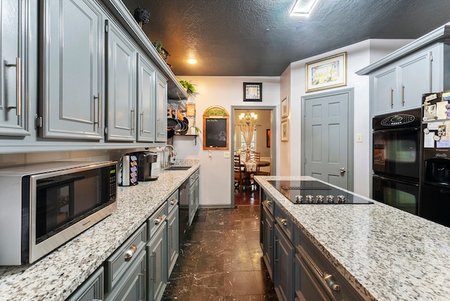 kitchen featuring gray cabinets, a sink, a textured ceiling, light stone countertops, and black appliances