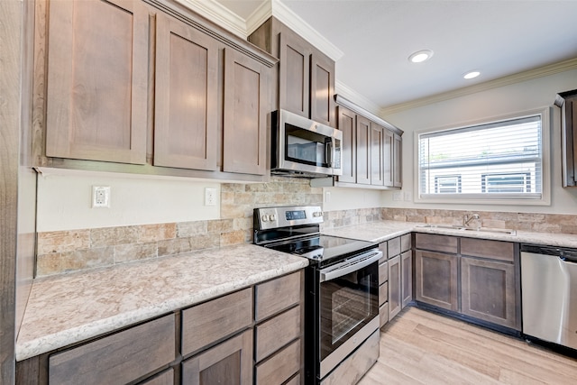 kitchen with light stone countertops, stainless steel appliances, light wood-type flooring, crown molding, and sink