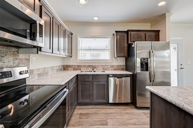 kitchen with appliances with stainless steel finishes, light wood-type flooring, crown molding, dark brown cabinets, and sink