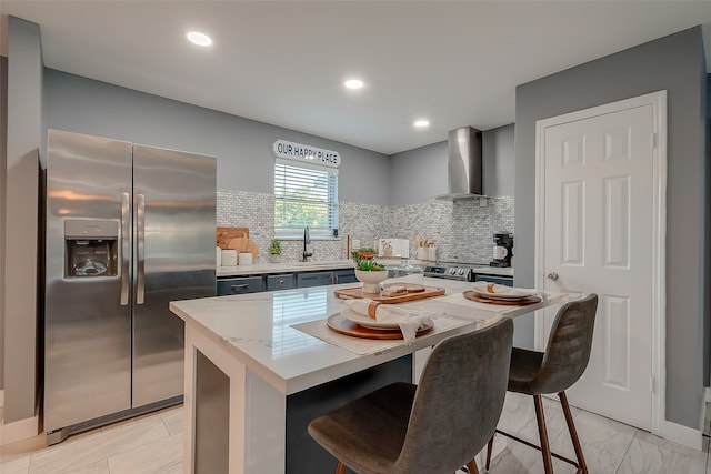 kitchen with a center island, appliances with stainless steel finishes, wall chimney range hood, and a breakfast bar area