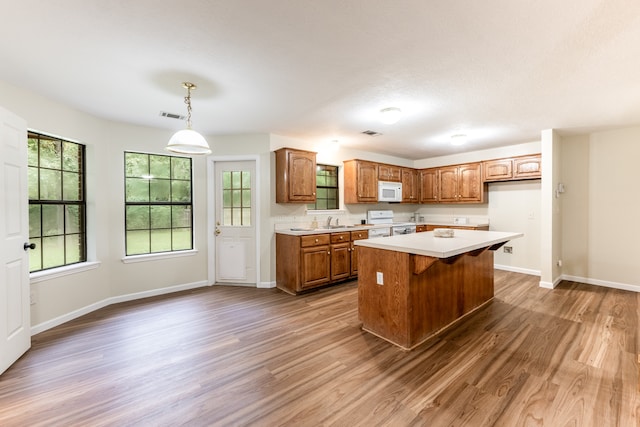 kitchen featuring hanging light fixtures, sink, white appliances, wood-type flooring, and a center island