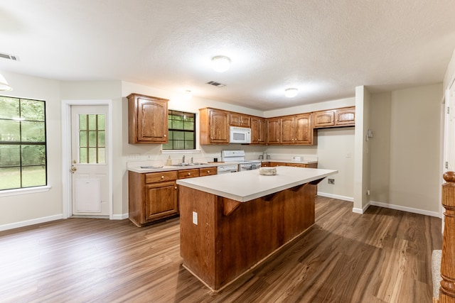 kitchen featuring dark wood-type flooring, white appliances, a kitchen island, a textured ceiling, and sink