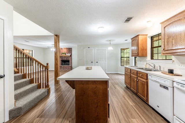 kitchen with a brick fireplace, a kitchen island, dishwasher, light wood-type flooring, and sink