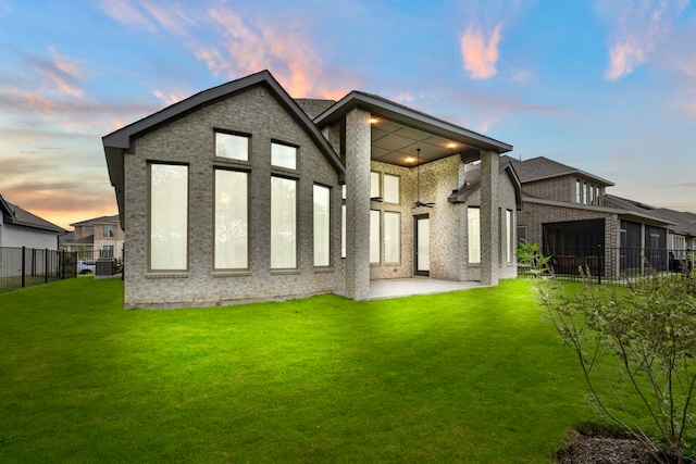 back house at dusk featuring a lawn and a patio