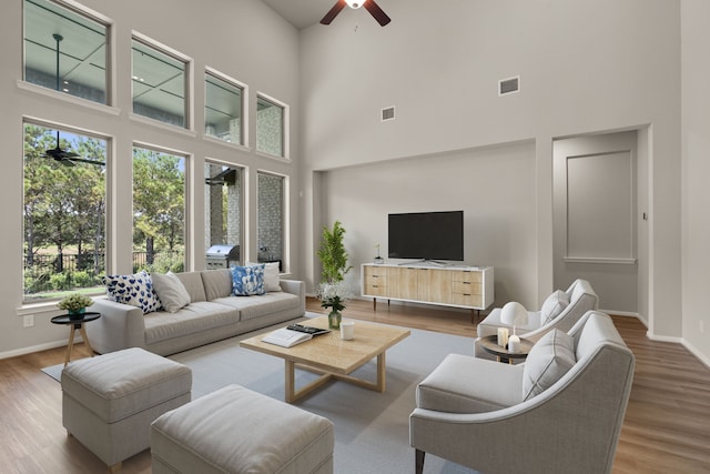 living room with ceiling fan, wood-type flooring, and a towering ceiling