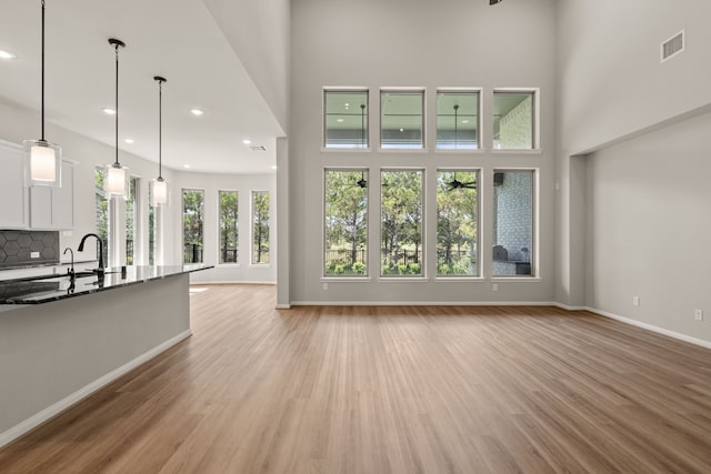 unfurnished living room featuring a high ceiling, light hardwood / wood-style flooring, and sink