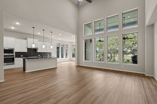 unfurnished living room with ceiling fan, light hardwood / wood-style floors, sink, and a towering ceiling