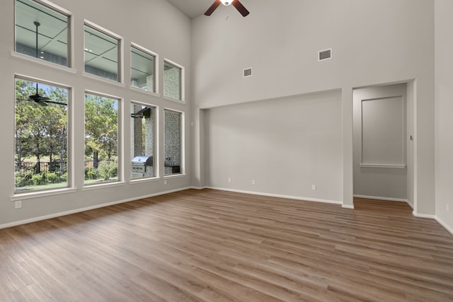 unfurnished living room with ceiling fan, a towering ceiling, and hardwood / wood-style flooring