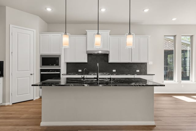 kitchen featuring light hardwood / wood-style floors, white cabinets, a center island with sink, and oven