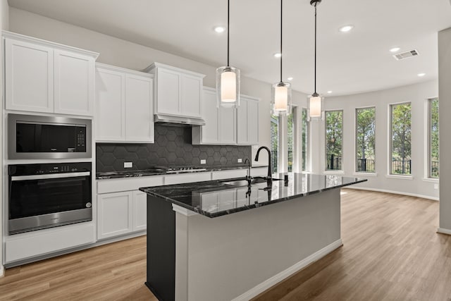 kitchen with white cabinetry, appliances with stainless steel finishes, a kitchen island with sink, hanging light fixtures, and sink