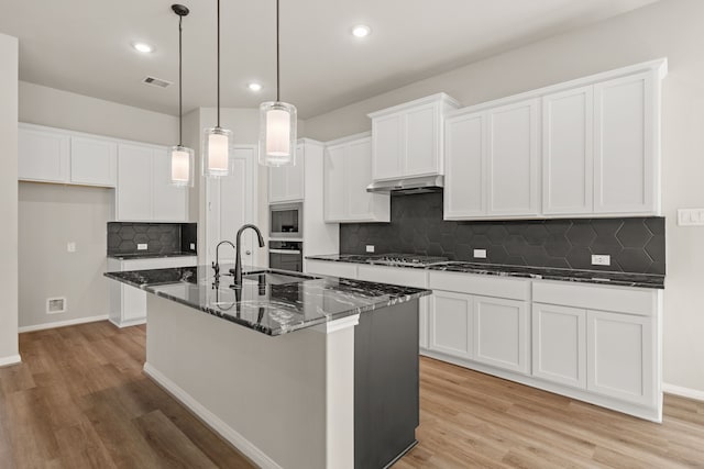 kitchen featuring white cabinets, appliances with stainless steel finishes, dark stone countertops, and a center island with sink