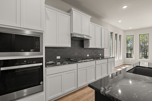 kitchen with white cabinets, backsplash, dark stone counters, and stainless steel appliances