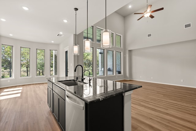 kitchen featuring dishwasher, pendant lighting, sink, a kitchen island with sink, and dark stone counters