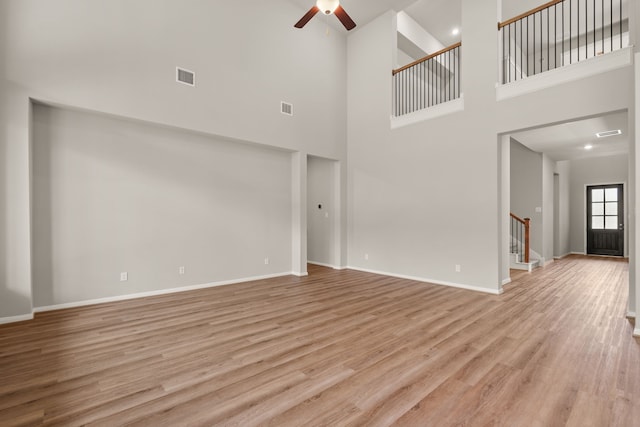 unfurnished living room featuring light wood-type flooring, ceiling fan, and a high ceiling