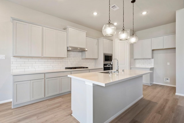 kitchen with a center island with sink, visible vents, white cabinets, light countertops, and a sink