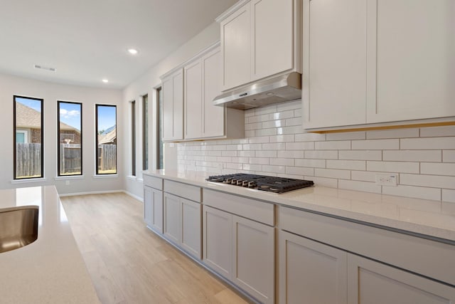 kitchen featuring visible vents, light wood-type flooring, under cabinet range hood, stainless steel gas stovetop, and white cabinetry