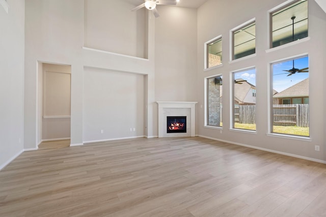 unfurnished living room featuring a ceiling fan, baseboards, light wood finished floors, and a premium fireplace