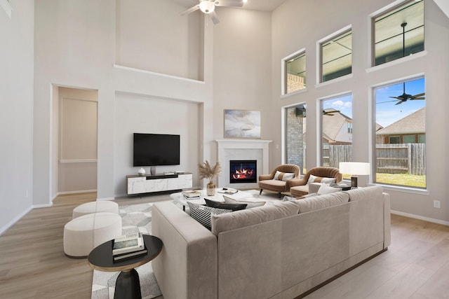 living area featuring light wood-type flooring, ceiling fan, baseboards, and a glass covered fireplace