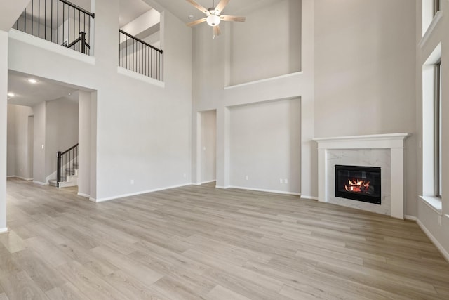 unfurnished living room featuring light wood-style flooring, a ceiling fan, a high end fireplace, baseboards, and stairs