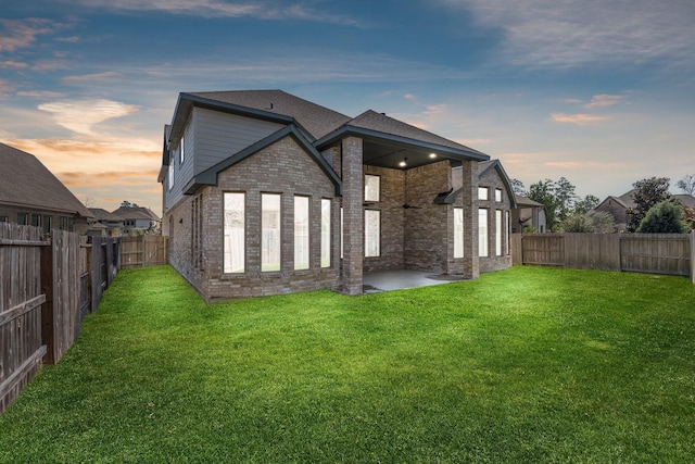 back of house at dusk featuring brick siding, a lawn, and a fenced backyard