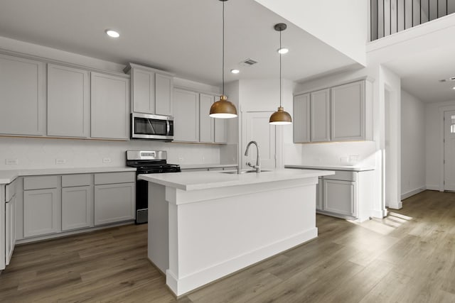 kitchen with appliances with stainless steel finishes, gray cabinets, pendant lighting, and an island with sink