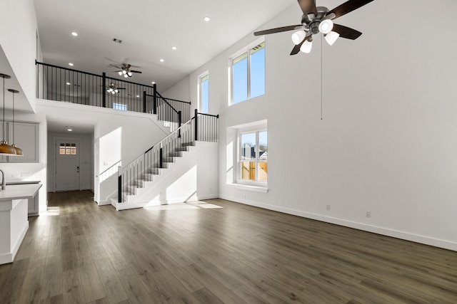 unfurnished living room featuring ceiling fan, dark hardwood / wood-style flooring, and a towering ceiling